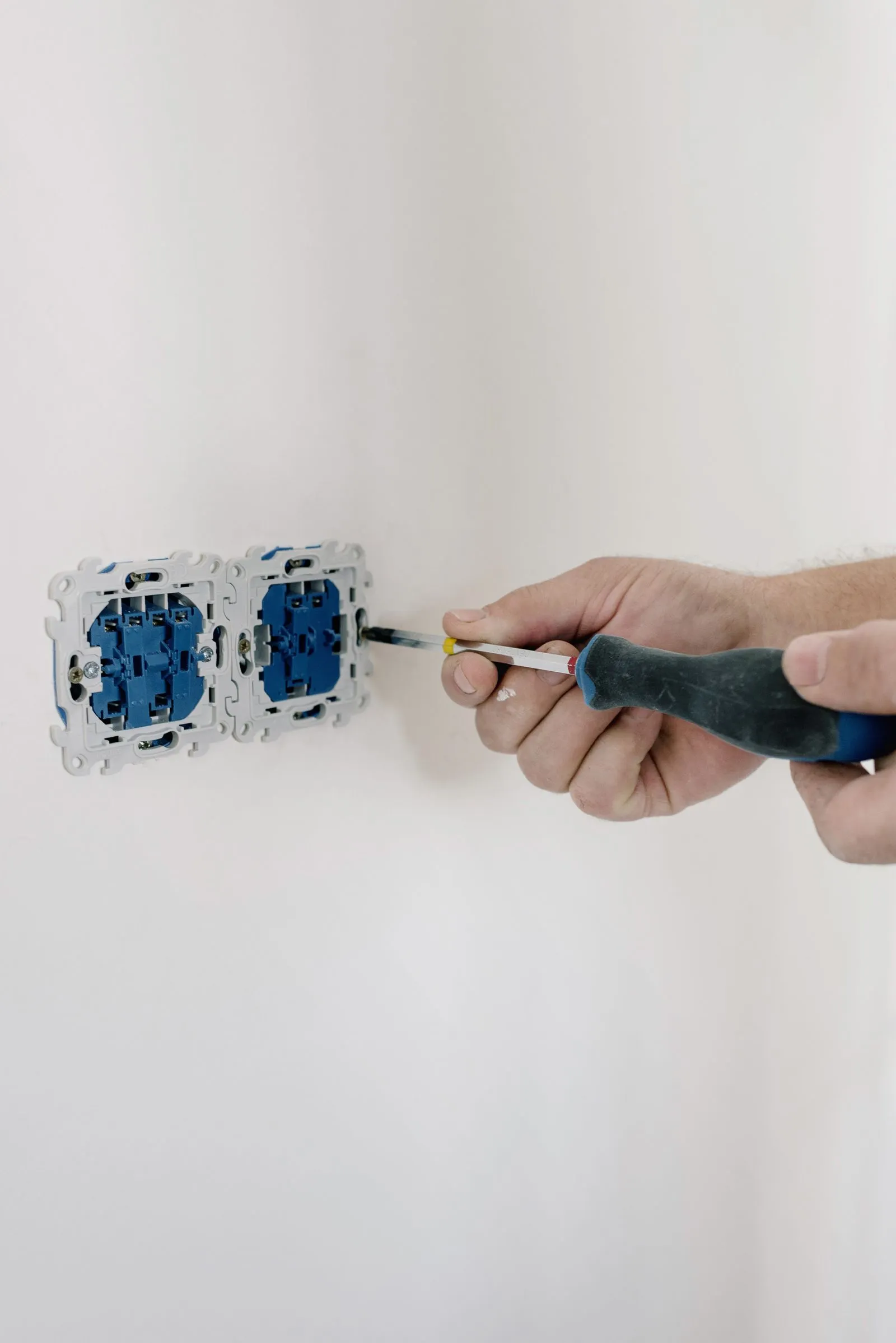 Electrician's hands tightening a wall outlet in a home