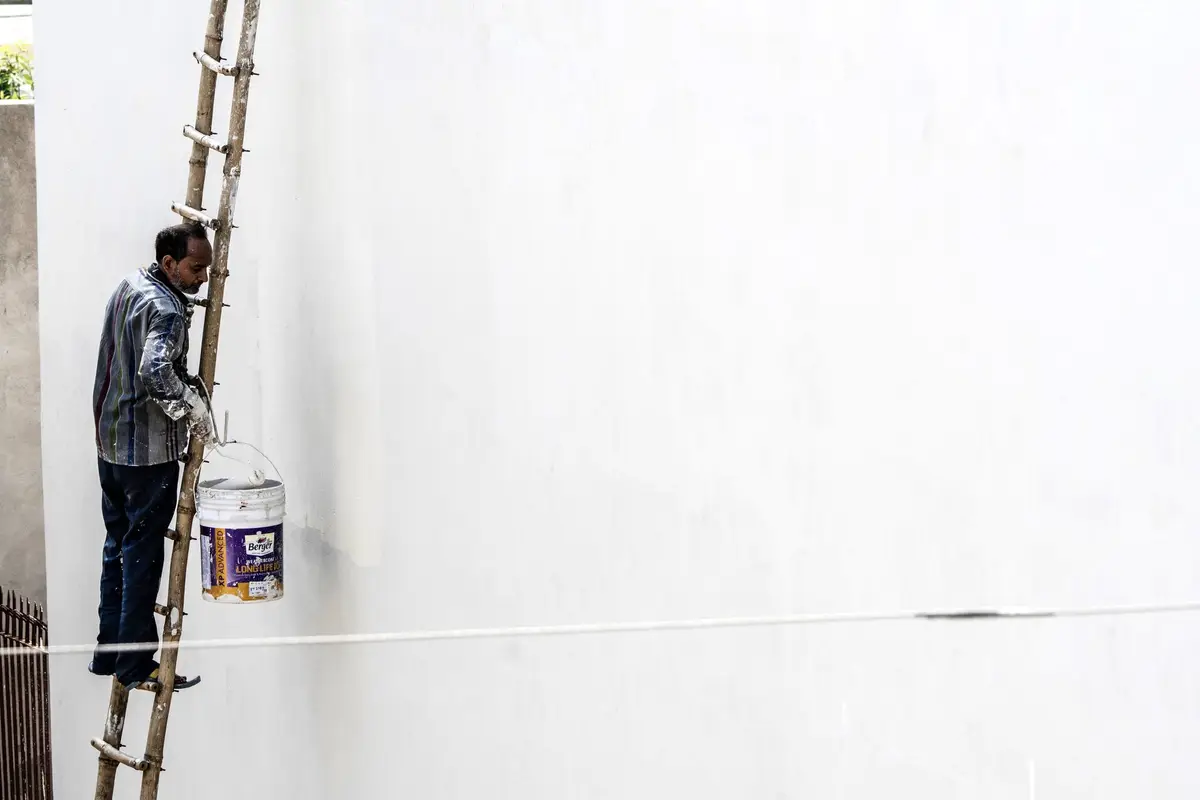 Painter on a ladder painting an outside wall