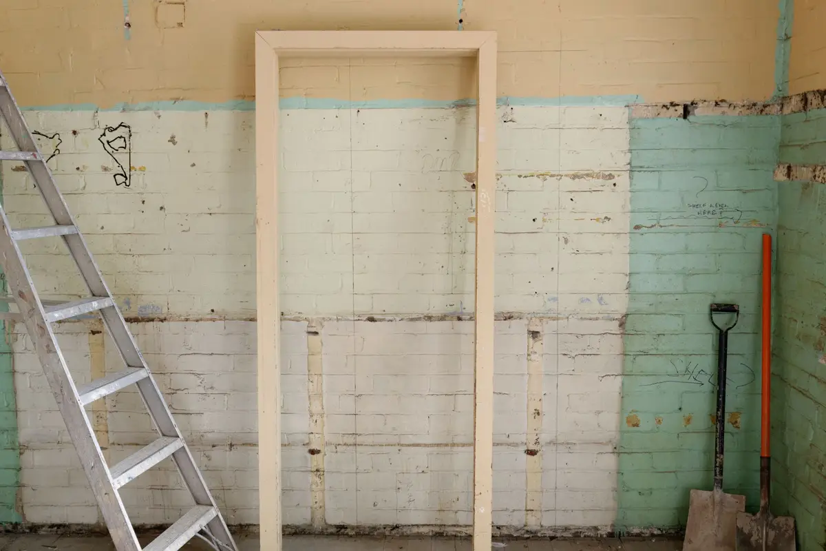 Room with walls opened up for repair, with a ladder and tools